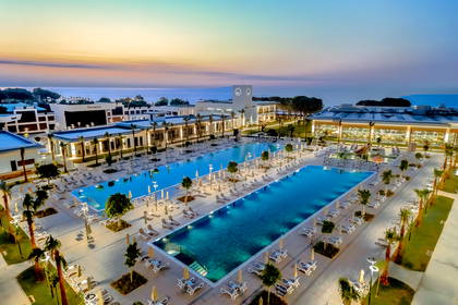 Luksusowy kompleks hotelowy z dwoma podświetlanymi basenami o zmierzchu, z widokiem na morze.