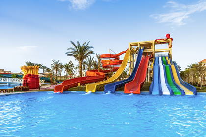 Słoneczny aquapark z wieloma kolorowymi zjeżdżalniami, basenem i palmami.