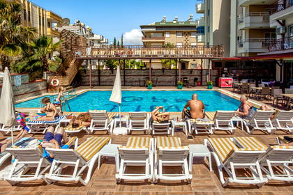 Ludzie wypoczywają na leżakach przy hotelowym basenie w słoneczny dzień.