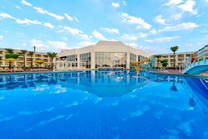 Duży basen w ośrodku wypoczynkowym, z hotelami i palmami w tle.