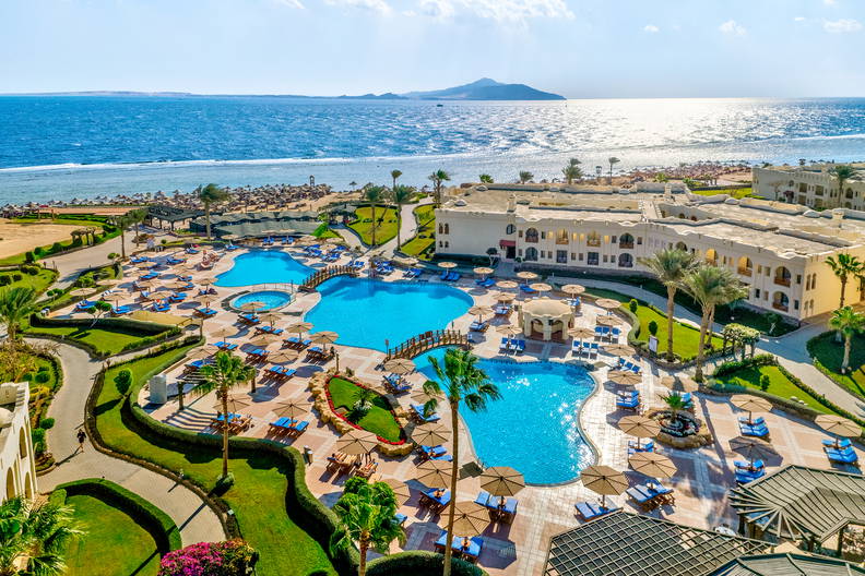 Hotel z dużymi basenami i palmami, położony przy piaszczystej plaży nad morzem.