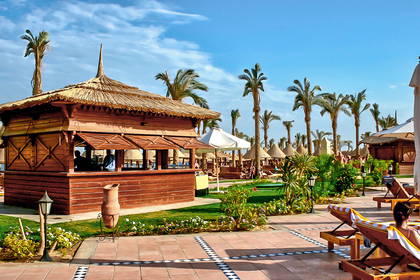 Drewniany bar z dachem ze strzechy na plaży, otoczony palmami i leżakami.