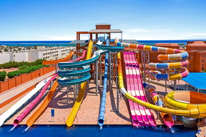 Duży aquapark z wieloma kolorowymi zjeżdżalniami, basenami i widokiem na morze.