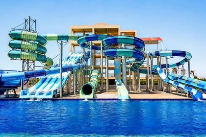 Aquapark z wieloma krętymi, niebiesko-zielonymi zjeżdżalniami wodnymi, które kończą się w dużym basenie.