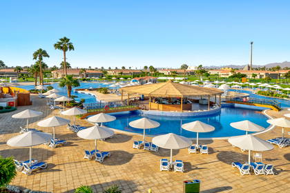 Duży basen hotelowy z barem na środku, otoczony leżakami, parasolami i palmami.