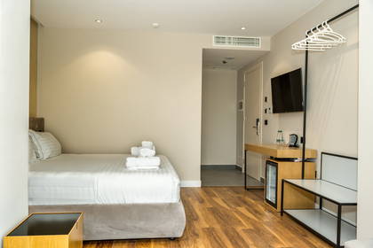 Nowoczesny pokój hotelowy z pojedynczym łóżkiem, drewnianą podłogą, biurkiem, telewizorem i minibarem.