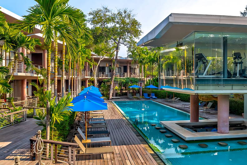 Basen hotelowy otoczony palmami i drewnianym tarasem.