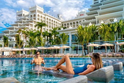 Para relaksuje się z drinkami w basenie luksusowego hotelu, w otoczeniu palm.