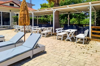 Słoneczne patio hotelowe z leżakami, białymi stolikami i parasolem krytym strzechą.