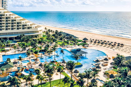 Luksusowy hotel przy plaży z kompleksem basenów, otoczony palmami, z widokiem na błękitny ocean.