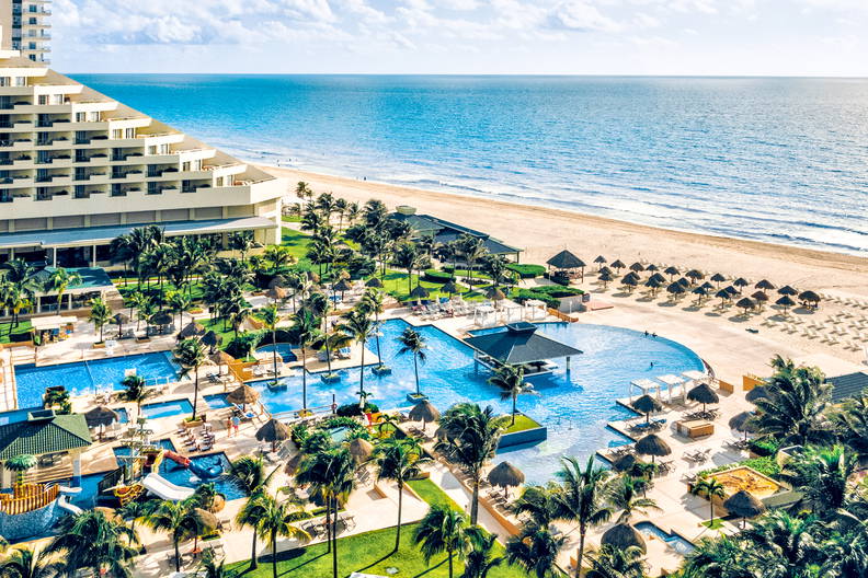 Luksusowy hotel przy plaży z kompleksem basenów, otoczony palmami, z widokiem na błękitny ocean.