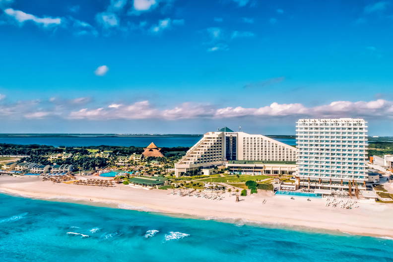 Kompleks hotelowy z lotu ptaka, położony przy białej, piaszczystej plaży i turkusowym oceanie.