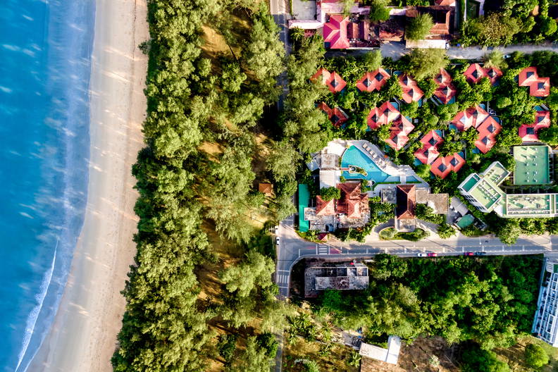 Widok z lotu ptaka na plażę i tropikalny kurort, które oddziela pas gęstych, zielonych drzew.