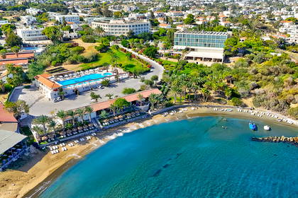 Widok z góry na kompleks hotelowy z basenem, położony przy piaszczystej plaży i turkusowej zatoce.