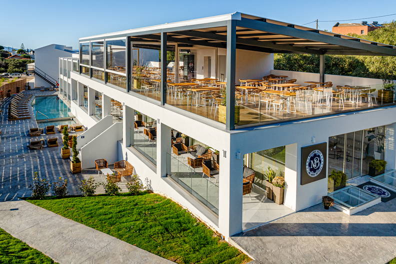 Nowoczesny, biały hotel z restauracją na tarasie i basenem.