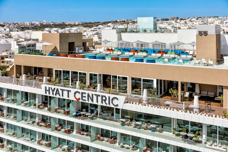 Basen z kolorowymi leżakami na dachu hotelu Hyatt Centric, z widokiem na panoramę miasta.
