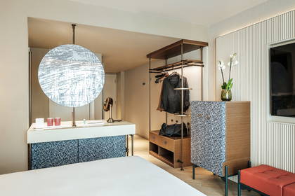 Nowoczesny pokój hotelowy z otwartą szafą, toaletką z okrągłym lustrem i wzorzystymi meblami.