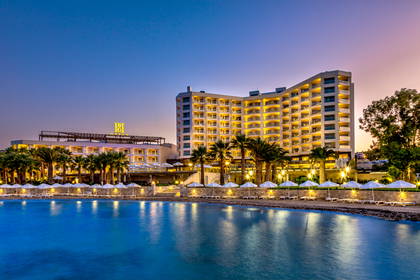 Oświetlony hotel przy plaży z palmami o zmierzchu.