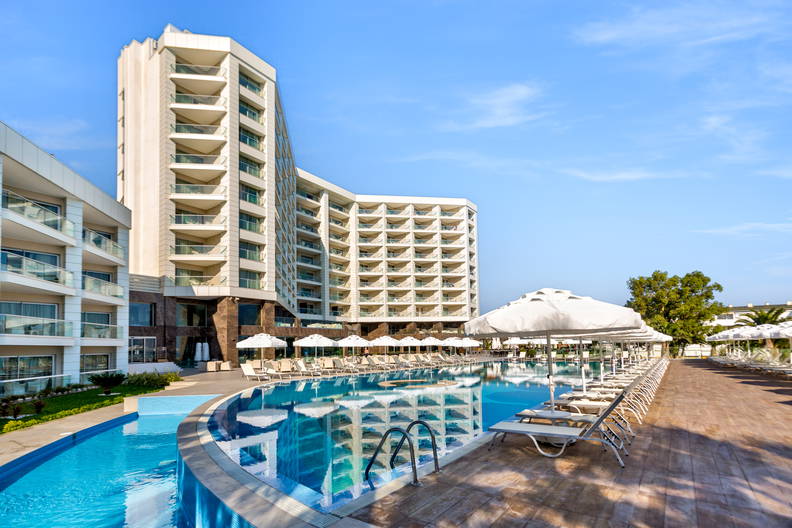 Nowoczesny hotel z dużym basenem, wokół którego ustawiono leżaki i białe parasole.