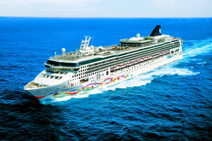 Duży statek wycieczkowy Norwegian Star z kolorowymi gwiazdami na kadłubie płynie po błękitnym oceanie.