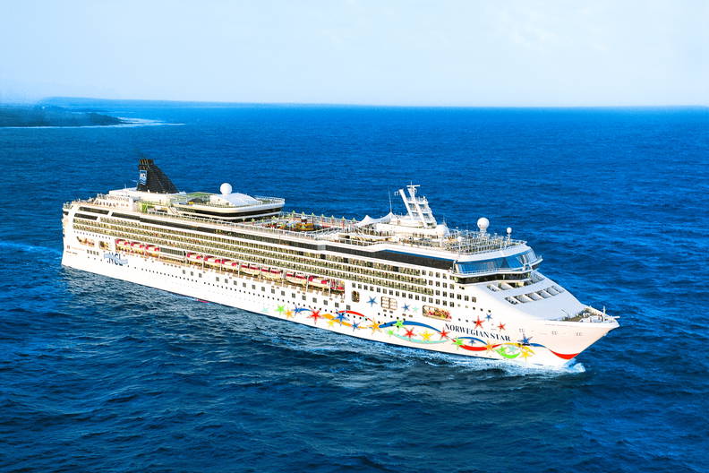 Statek wycieczkowy Norwegian Star płynie po błękitnym oceanie. Na horyzoncie widać zarys lądu.