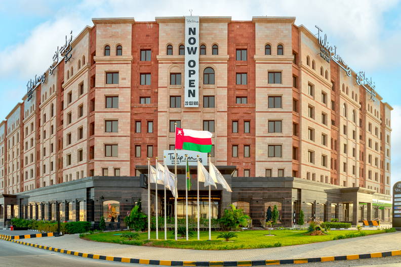 Nowoczesny hotel Tulip Inn z banerem „NOW OPEN” i flagą Omanu przed wejściem.