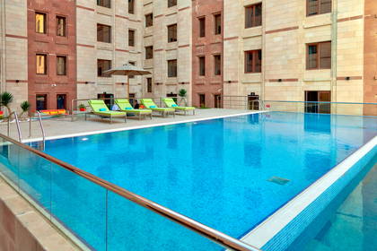 Zewnętrzny basen hotelowy z zielonymi leżakami na tle kamiennego budynku.