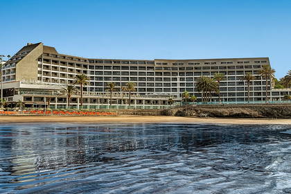 Hotel na plaży z palmami i turkusowym niebem w tle.