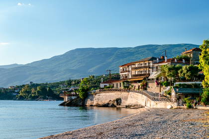 Kamienista plaża z widokiem na nadmorskie miasteczko i zielone góry w słoneczny dzień.