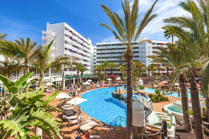 Kompleks hotelowy z basenem, palmami i leżakami.