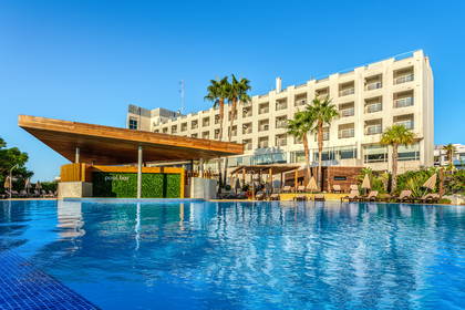 Duży basen hotelowy z błękitną wodą, palmami i barem.
