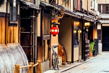 Wąska uliczka w Japonii z tradycyjnymi, drewnianymi domami, czerwoną latarnią i rowerem.