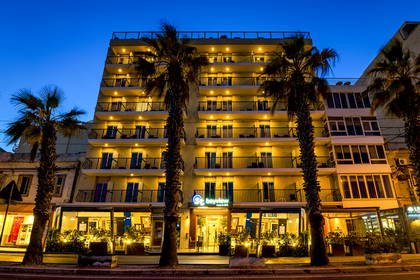 Oświetlona nocą fasada hotelu Bayview z rzędami balkonów i palmami.