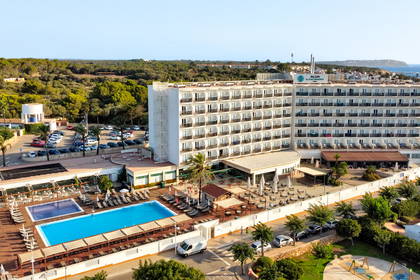 Widok z lotu ptaka na duży hotel z basenem, położony na wybrzeżu, w otoczeniu drzew.