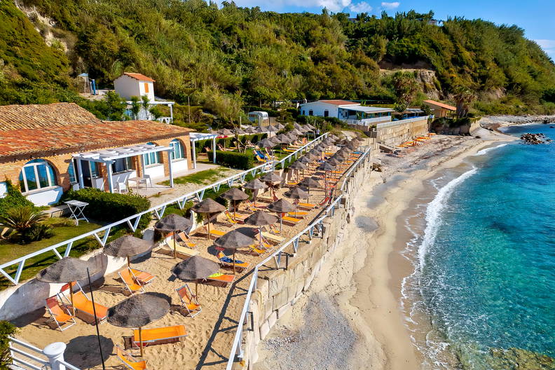 Piaszczysta plaża z rzędami parasoli nad turkusowym morzem.