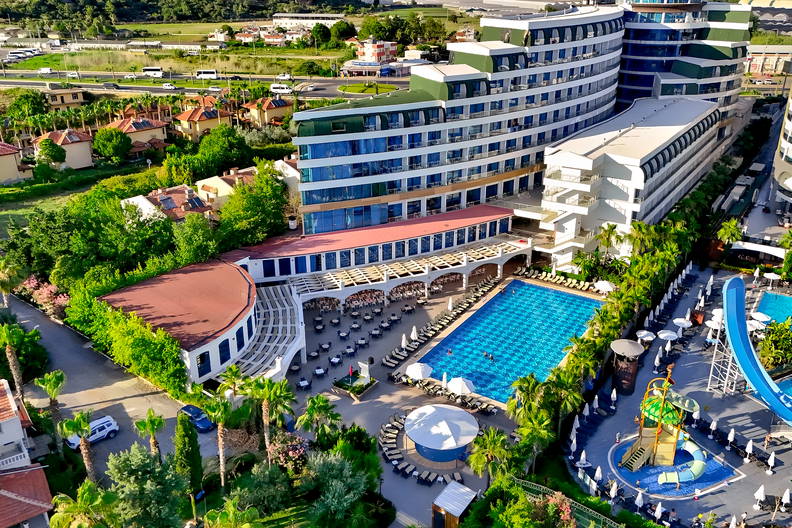 Widok z góry na duży kompleks hotelowy z basenami, zjeżdżalnią wodną i palmami.
