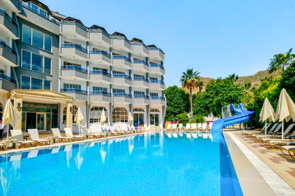 Basen z niebieską zjeżdżalnią, leżakami i parasolami przy dużym budynku hotelowym.