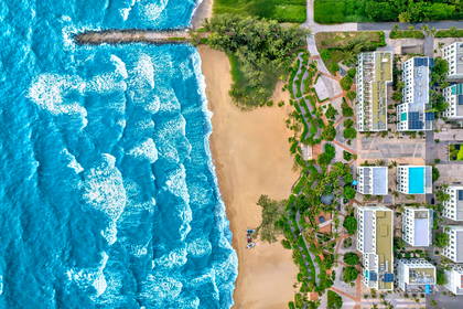 Widok z lotu ptaka na turkusowe morze, piaszczystą plażę i nadmorski kompleks hotelowy z basenami.