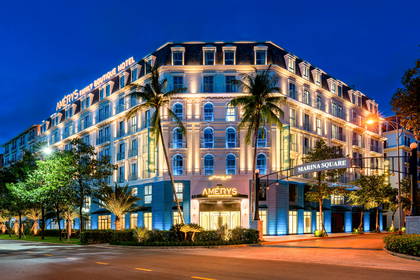 Elegancki budynek hotelu Amérys oświetlony nocą. Przed wejściem rosną palmy.
