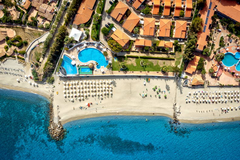 Widok z lotu ptaka na kurort z basenami przy piaszczystej plaży nad turkusowym morzem.