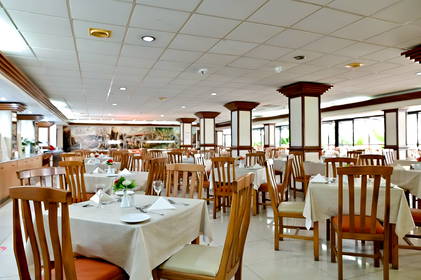 Przestronne wnętrze restauracji z rzędami nakrytych stolików z drewnianymi krzesłami i jasnymi obrusami.