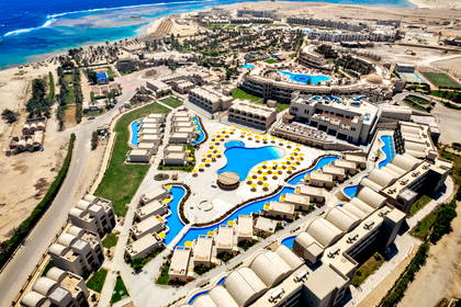 Widok z lotu ptaka na duży ośrodek hotelowy z basenami, położony przy piaszczystej plaży nad turkusowym morzem.