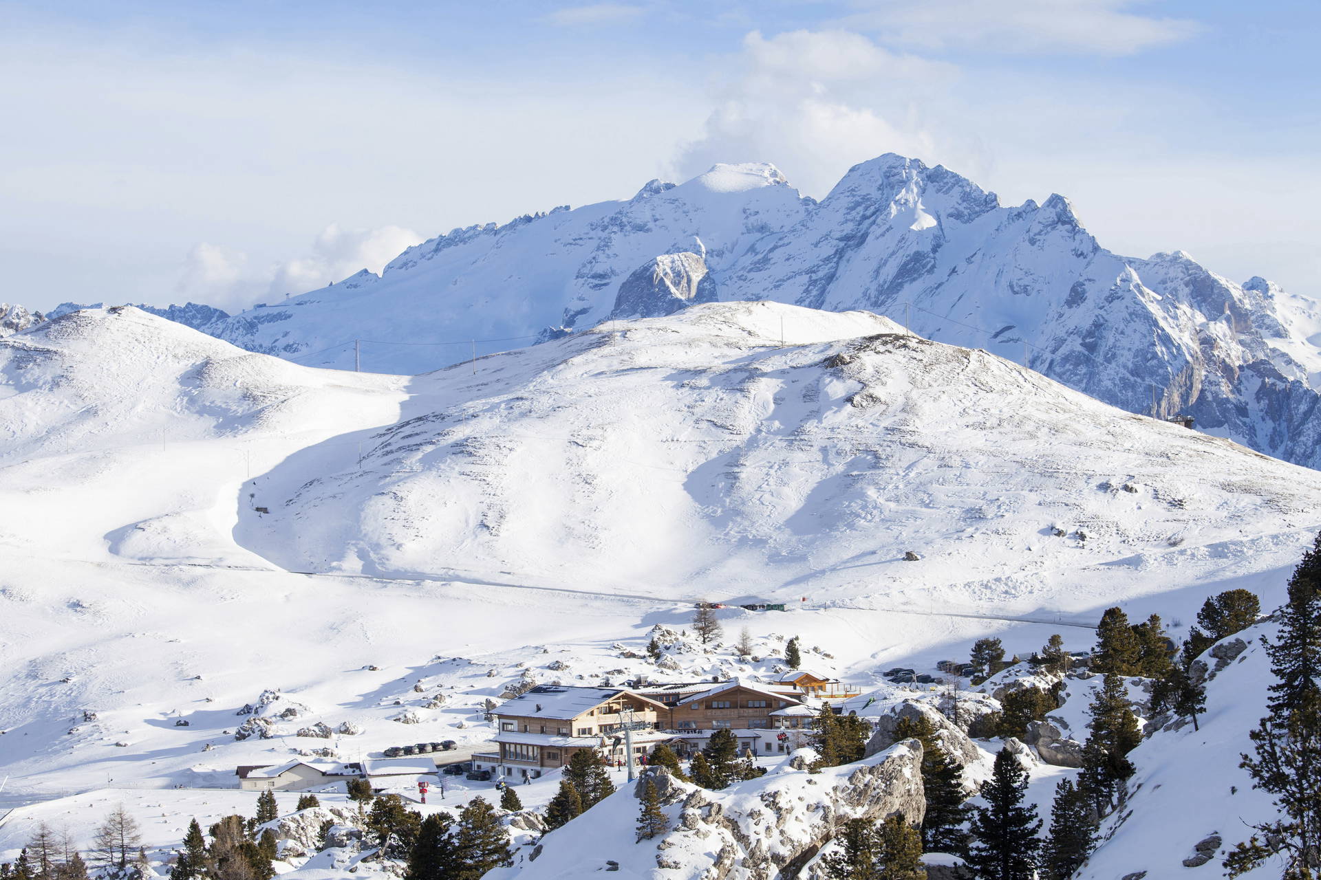 Zimowy krajobraz w Dolomitach. Na zdjęciu budynki na tle ośnieżonych gór.