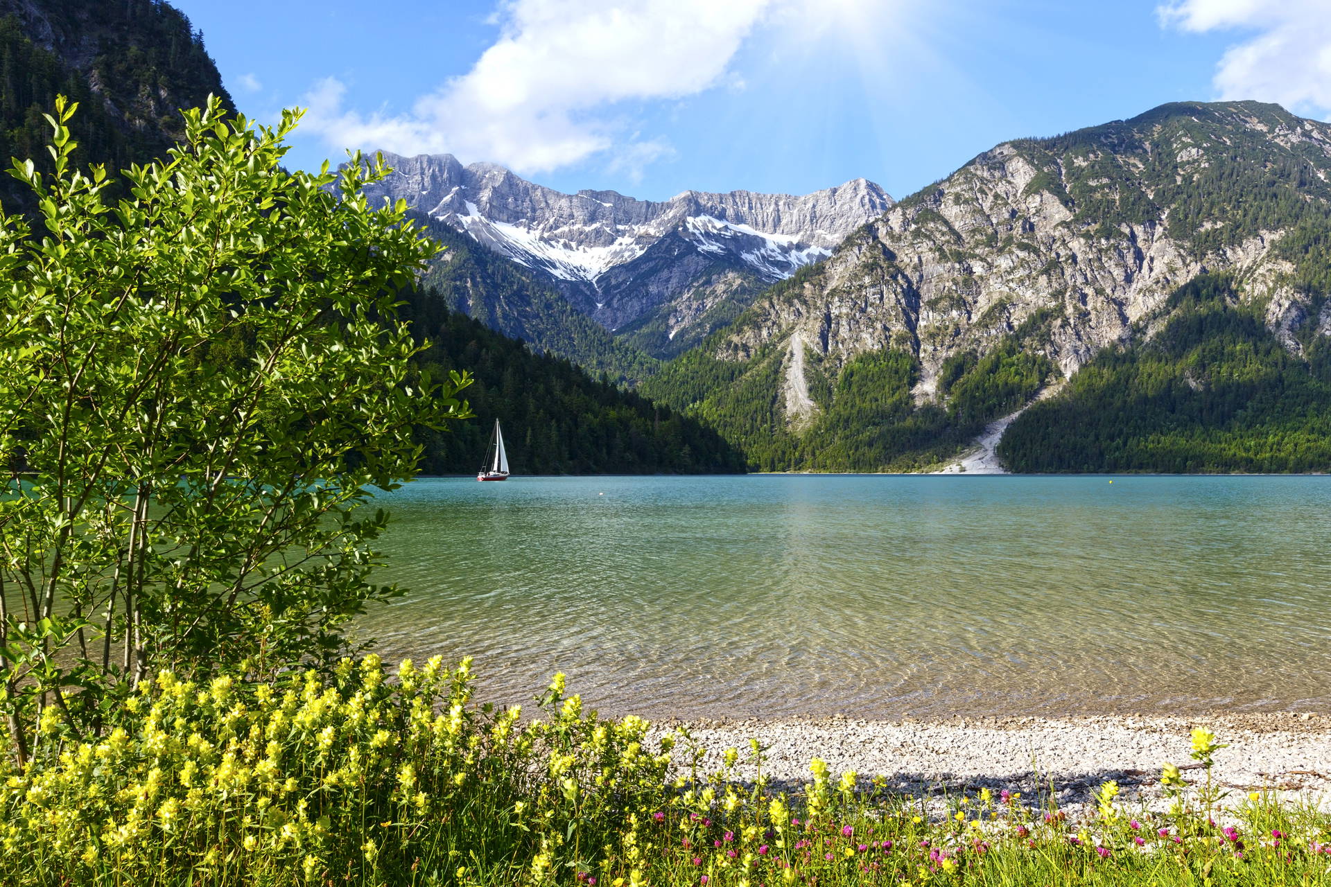 Jezioro z żaglówką w otoczeniu gór.