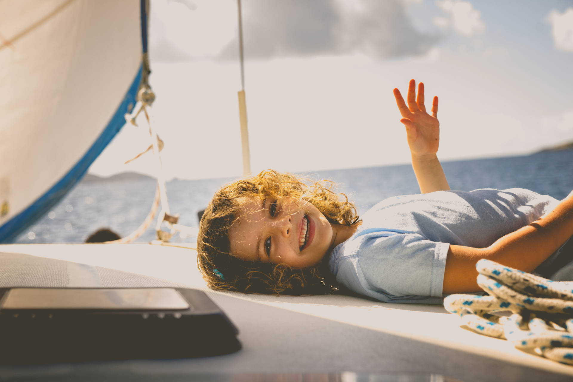 Uśmiechnięta dziewczynka z kręconymi włosami leży na łodzi i macha ręką.