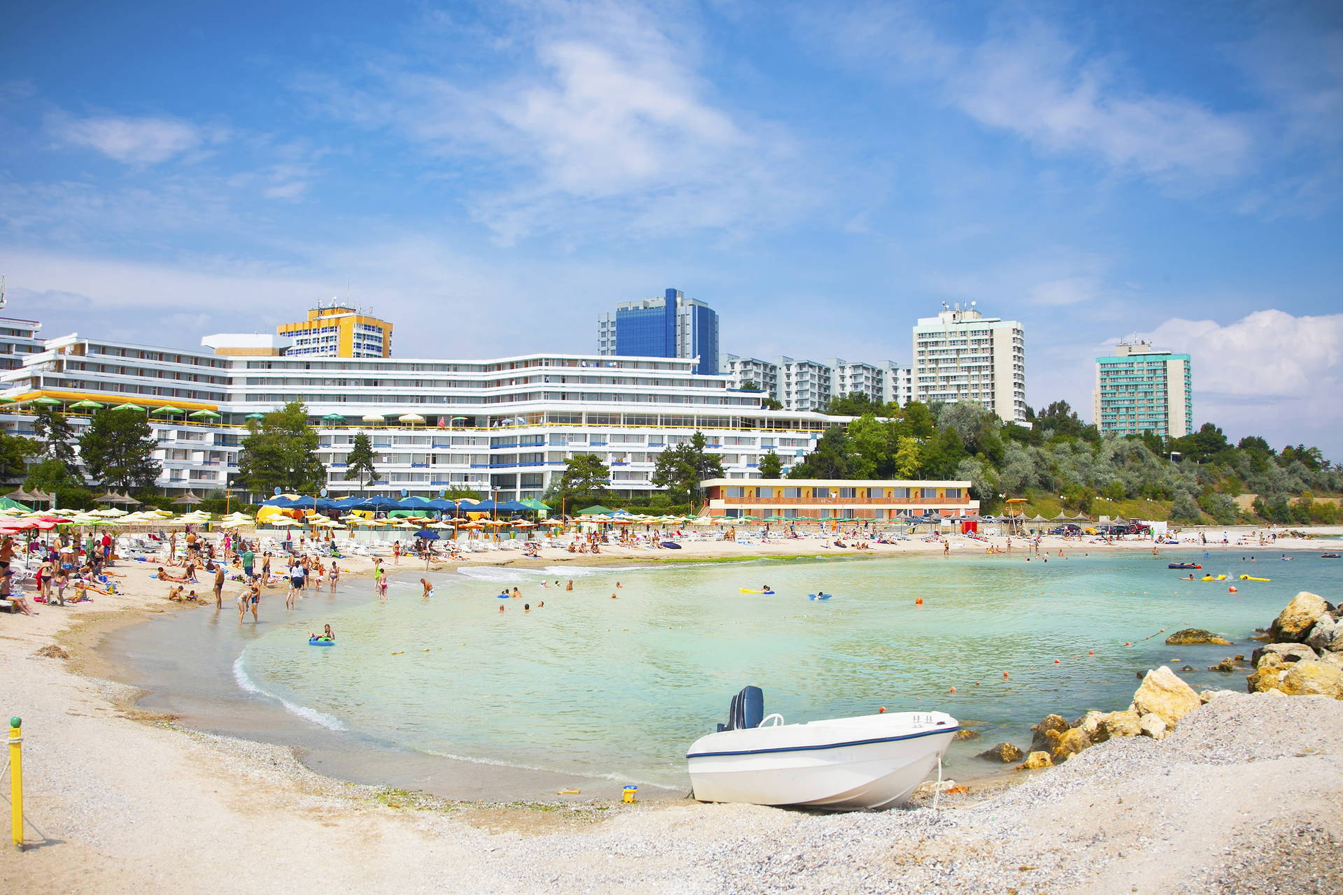 Zatłoczona plaża i biały jacht na pierwszym planie.