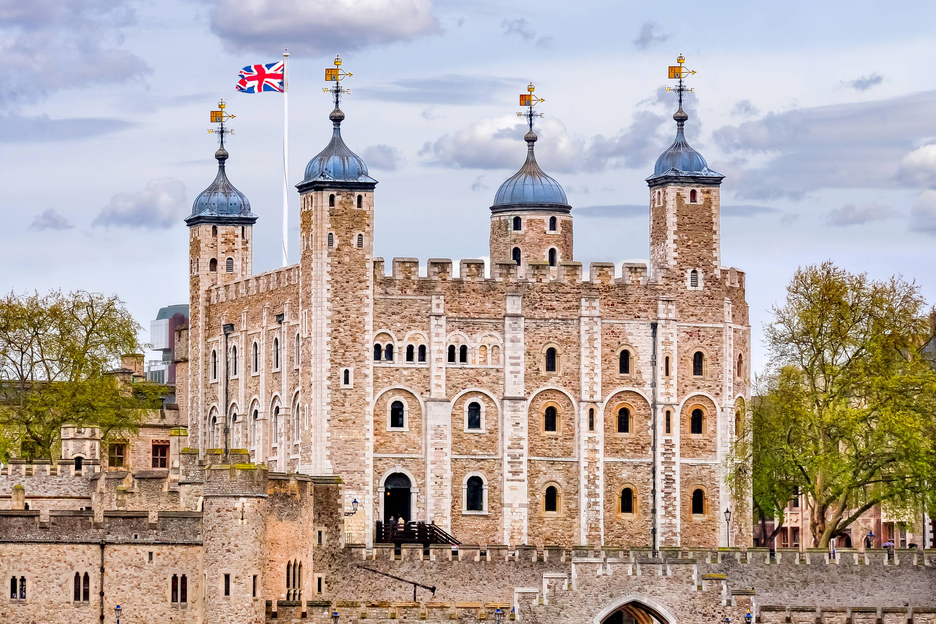 Tower of London, kamienna forteca z czterema wieżami, nad którą powiewa brytyjska flaga.