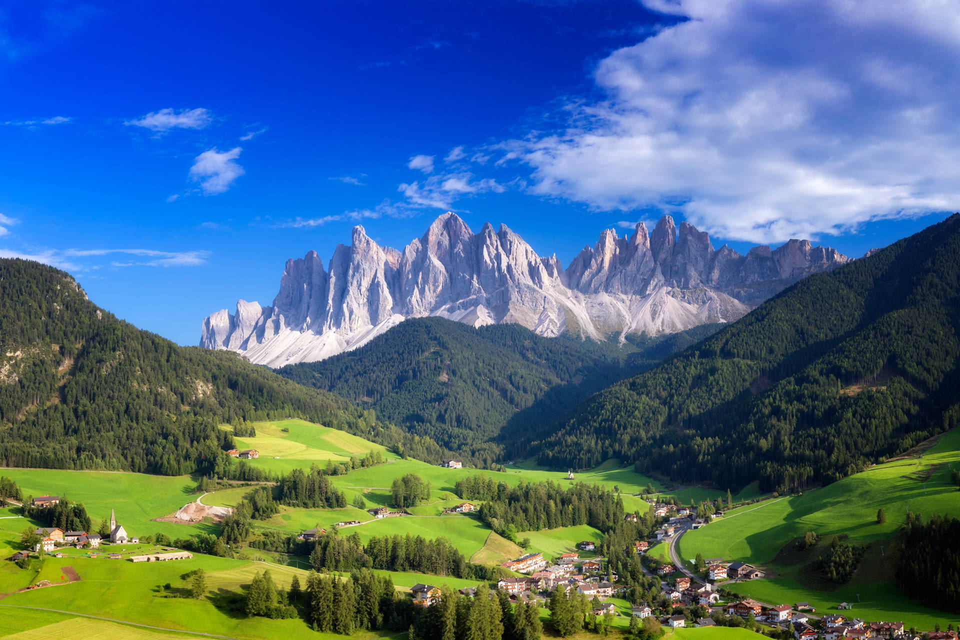 Widok na dolinę Val di Funes w Dolomitach z charakterystycznymi szczytami Odle, zielonymi łąkami i małą miejscowością.