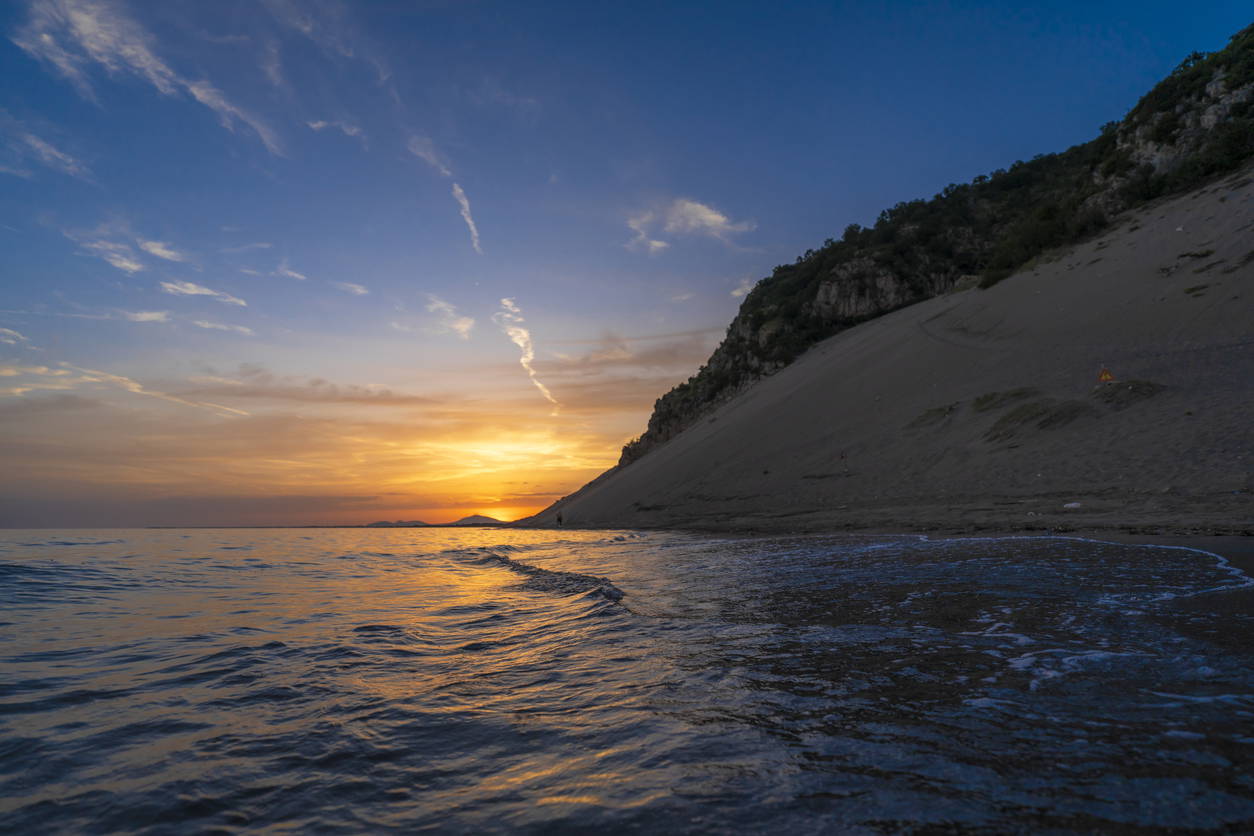 Zachód słońca na piaszczystej plaży ze stromą wydmą.