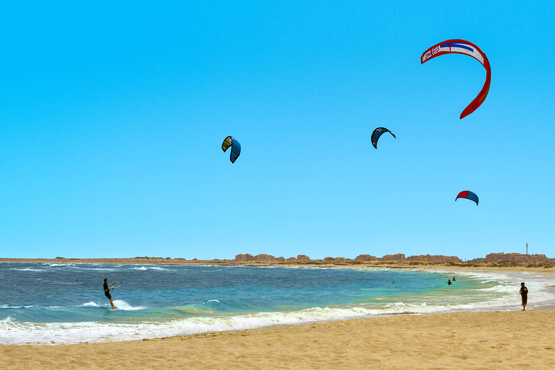Plaża z kitesurferami. W tle widoczne budynki.